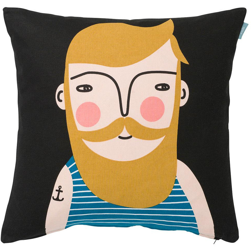 Black cushion cover with man's face with mustard yellow hair, beard and mustache. He wears a blue and white tank top with a tattoo of an anchor on his arm.