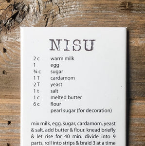 White magnet with Nisu recipe in brown text resting on a brown wooden table.
