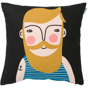 Black cushion cover with man's face with mustard yellow hair, beard and mustache. He wears a blue and white tank top with a tattoo  of an anchor on his arm.