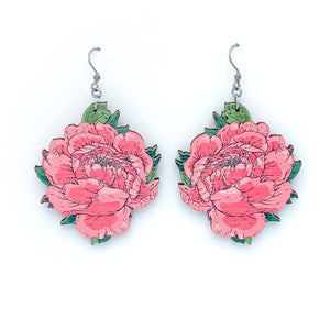 Photo of two pinkish red wooden peony earrings with green leafs on a white background. 