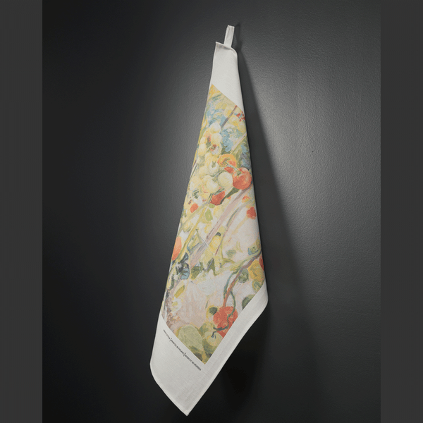 Tea towel with a design of a painting of red and green tomatoes on vines with a white background. Hanging on a black wall.